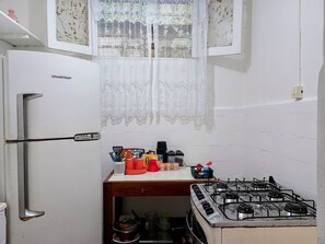A compact kitchen with a refrigerator, a gas stove, and a window with lace curtains.