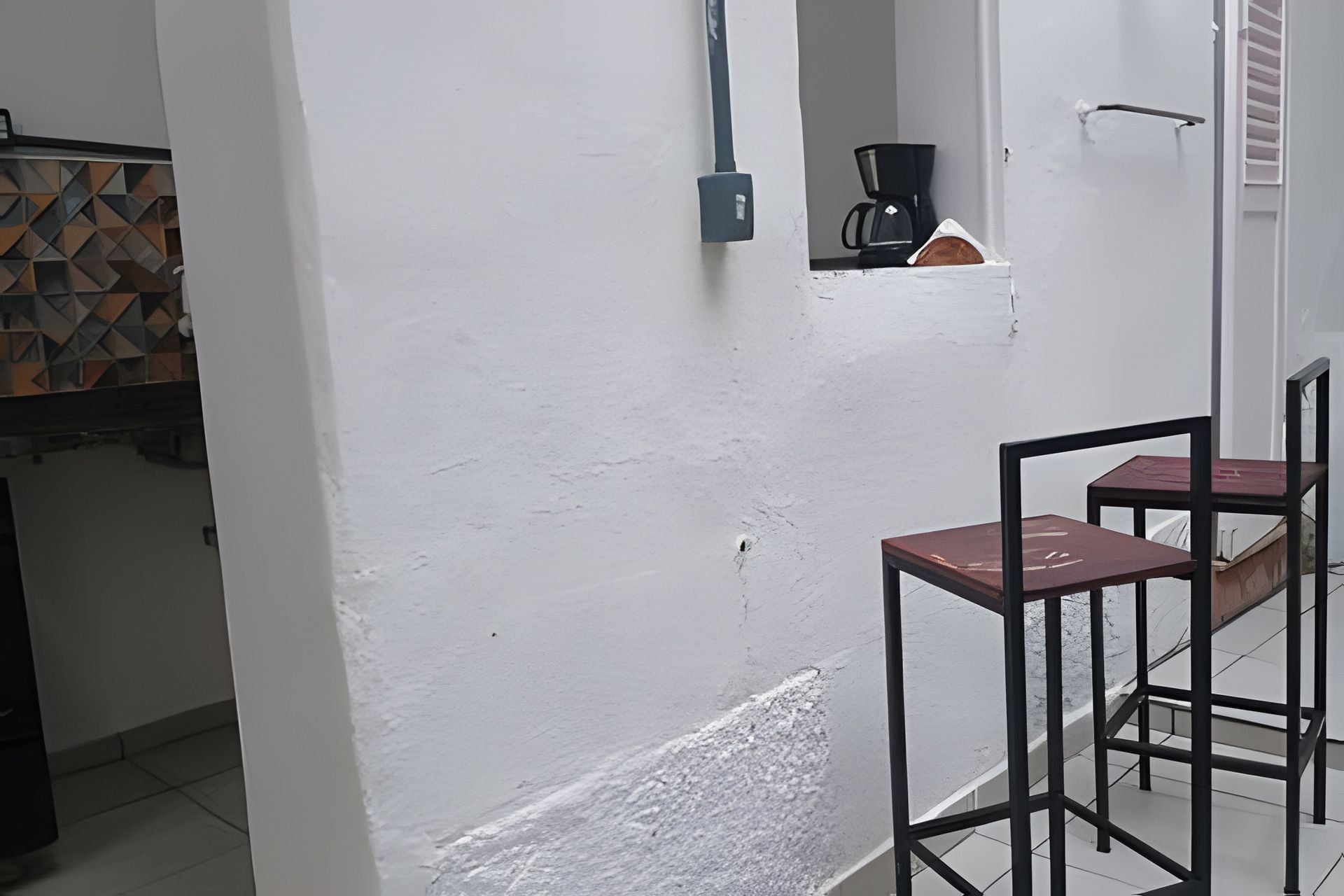 Quarto com parede branca, cafeteira e duas cadeiras.
