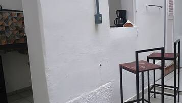 Quarto com parede branca, cafeteira e duas cadeiras.