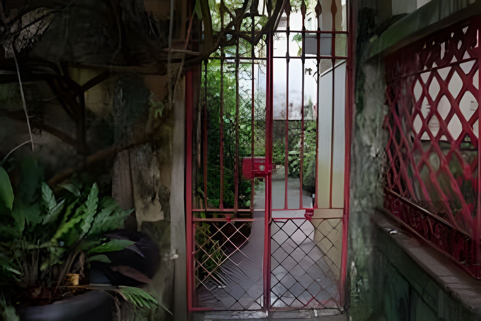Uma entrada gradeada com portão de metal, cerca vermelha e um caminho que leva a um edifício.