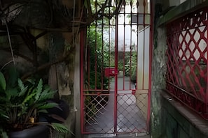A gated entrance with a metal gate, a red fence, and a pathway leading to a building.