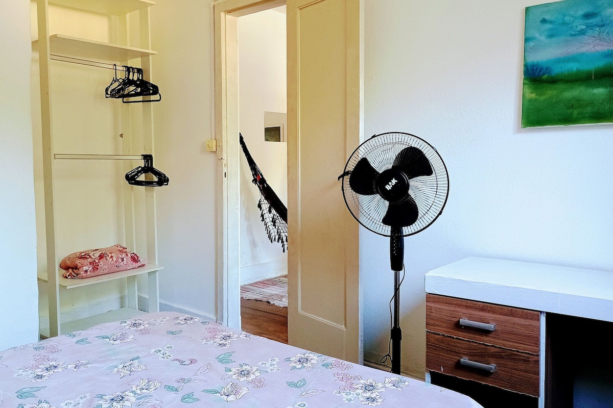 A bedroom with a bed, a fan, a wooden dresser, and a closet with shelves.