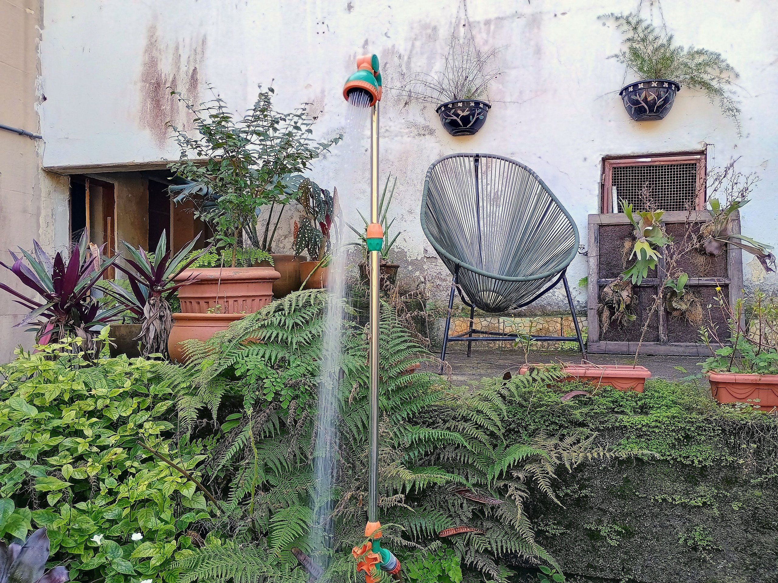 Um jardim com um elemento de água, plantas em vasos e uma cadeira.
