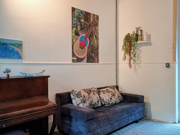 A room with a piano, a sofa with floral cushions, and wall art including a guitar and a painting.