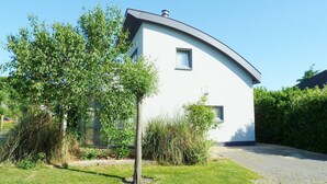 Ein modernes Haus mit gewundener Dachform, einem kleinen Fenster und einem Baum im Vordergrund.