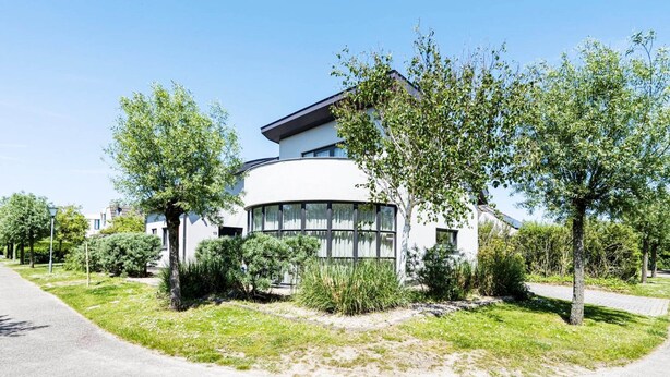 Ein modernes Gebäude mit einer geschwungenen Fassade, umgeben von Grün und blauem Himmel.