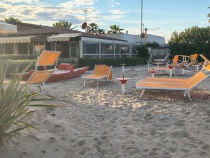 Una zona sulla spiaggia con lettini e una piccola barca con la scritta 'SALVADORA' sulla sabbia.