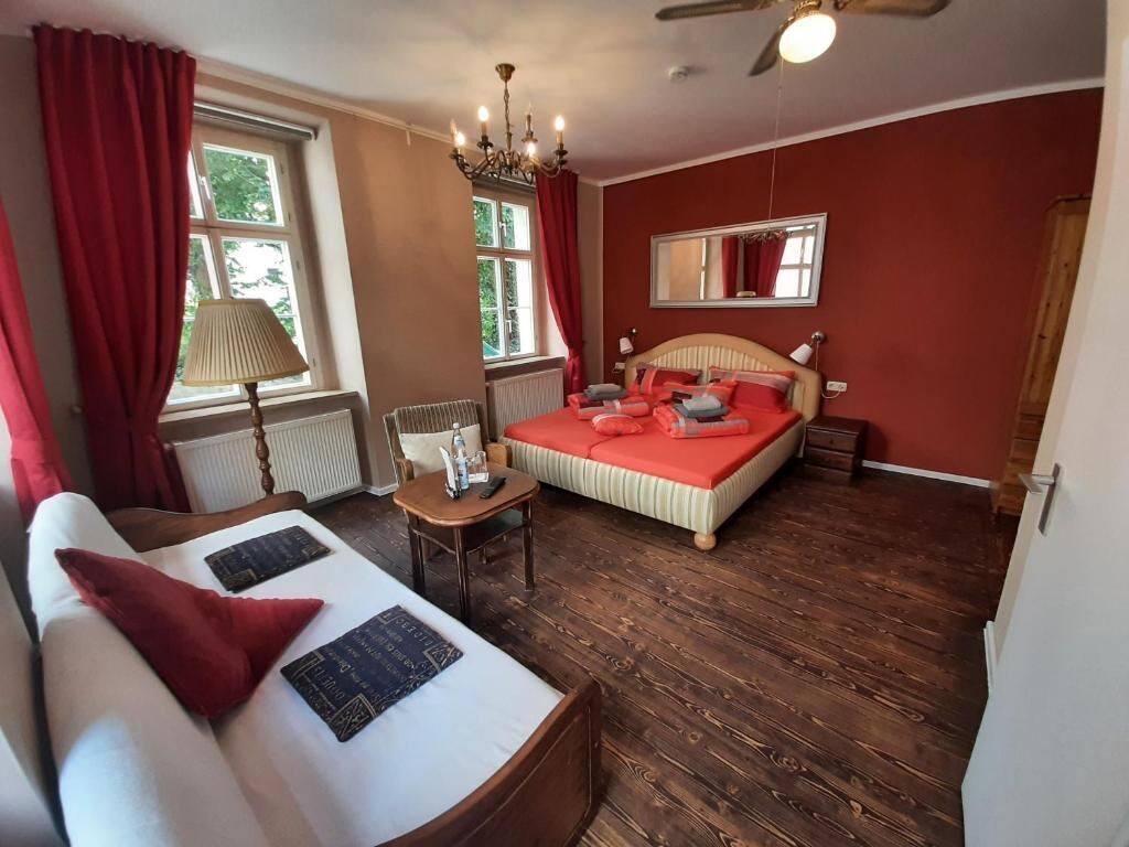 Quarto com cama, sofá, mesa pequena, luminária, janela e ventilador de teto.