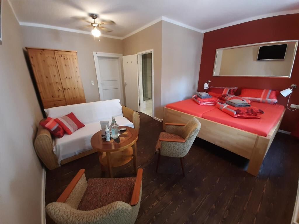 Une chambre d’hôtel avec un lit, un canapé, une chaise, une petite table et un ventilateur de plafond.