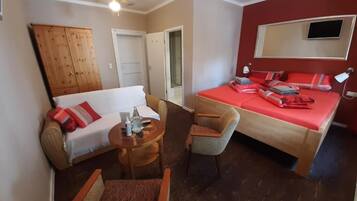 A hotel room with a bed, a sofa, a chair, a small table, and a ceiling fan.