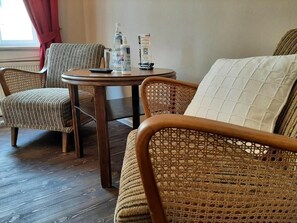 A room with wicker furniture, a round table with a remote control, and a bed with a quilted pillow.