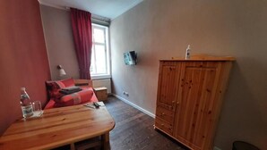 A room with a wooden table, a sofa, a cabinet, a TV, and a window with curtains.