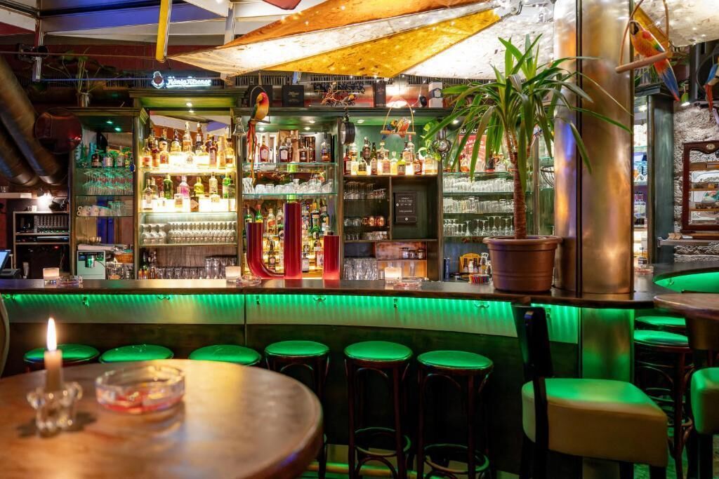 Eine Bar mit Barhocker, Flaschenregalen und einer beleuchteten Theke in Grün.