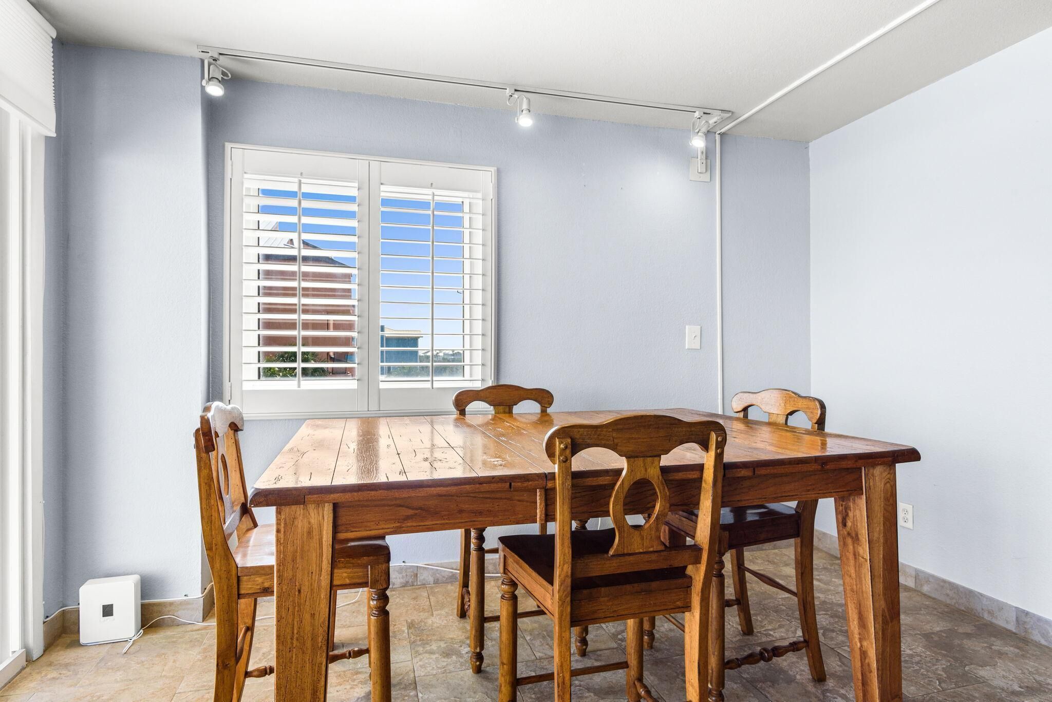 A dining area with a wooden table and chairs, a window with blinds, and a light switch on the wall.