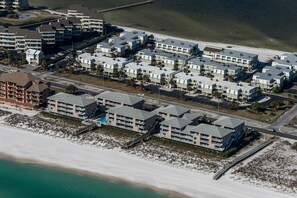 Ein Luftbild eines Küstenhotels mit mehreren Gebäuden, einem Strand und einem Steg.