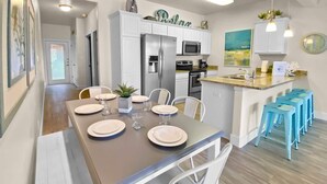 Une cuisine moderne avec des armoires blanches, un réfrigérateur en acier inoxydable, un four à micro-ondes et une cuisinière. On y trouve une table à manger mise avec des assiettes, des verres et une plante.