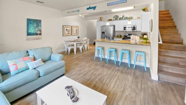 Un salon moderne comprenant un canapé, une table basse et un coin cuisine avec des tabourets de bar.