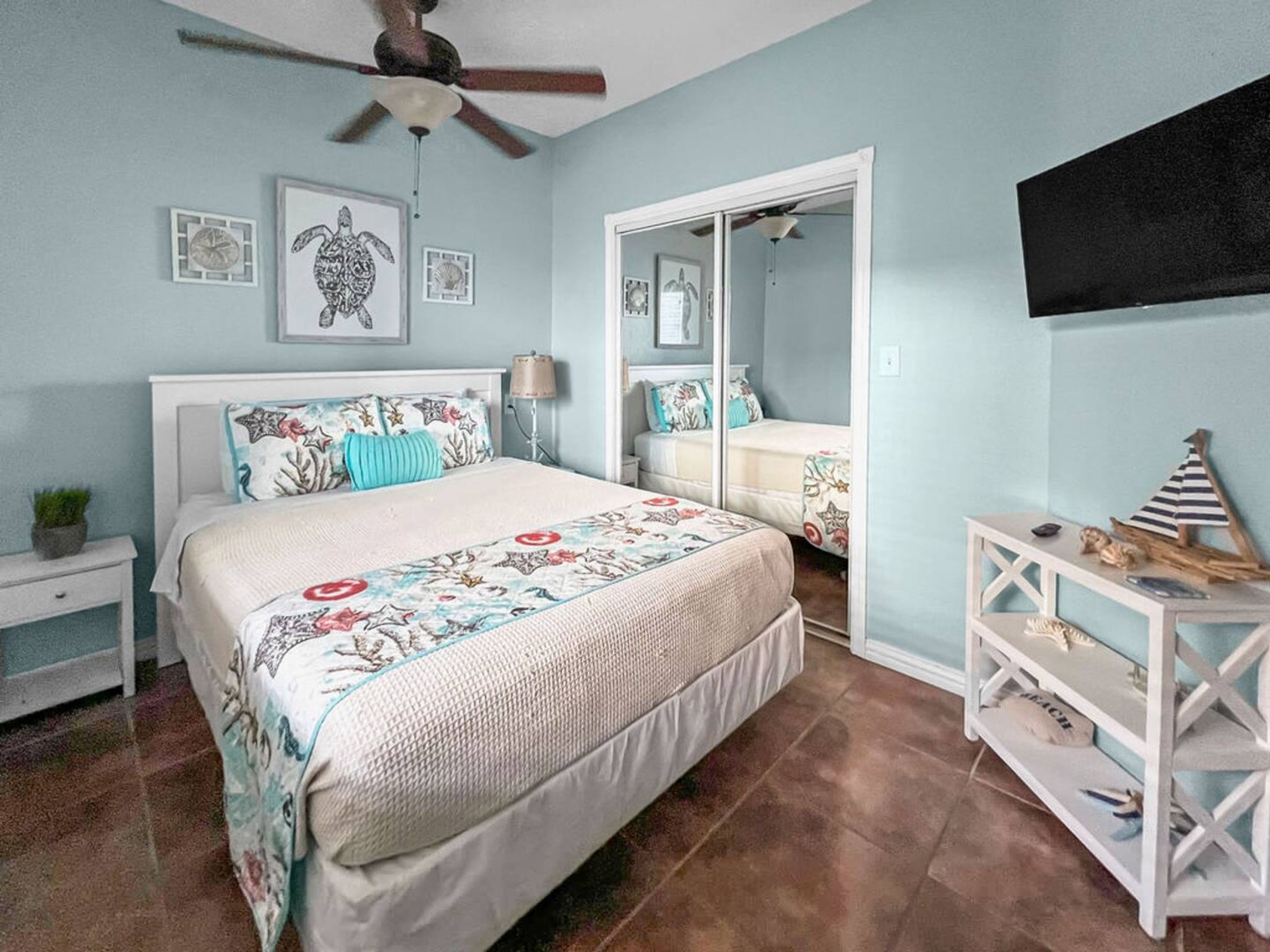A bedroom with a bed, a nightstand, a dresser, a ceiling fan, and a mirror.
