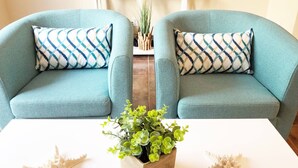 Una habitación con dos sillones azul verdosos, una mesa de centro blanca y una maceta de madera con plantas verdes.
