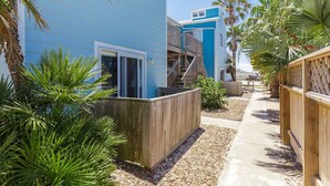 Un edificio costero con fachada azul, terraza de madera y palmeras.