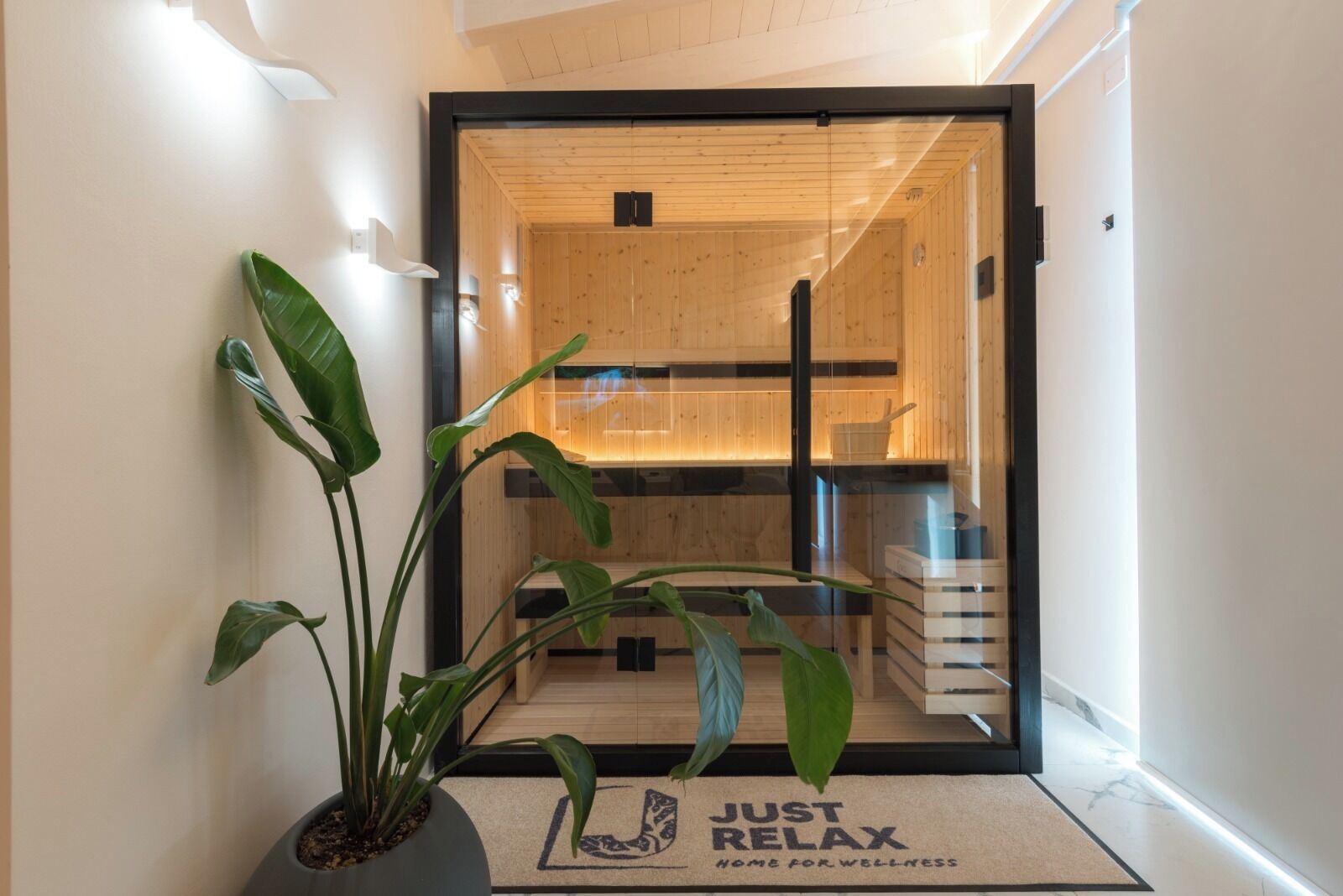 Un interior moderno con una pared de madera, una puerta de cristal y un felpudo con la inscripción 'JUST RELAX HOME FOR WELLNESS'.