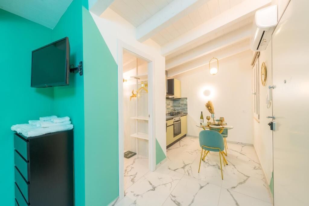 A compact kitchen with a dining area, a TV mounted on the wall, and a bathroom with a towel rack.