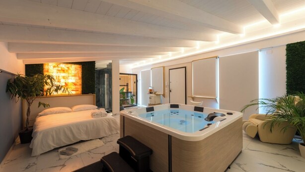 A modern bedroom with a large bed, a jacuzzi, and a small seating area. - Just Relax Home (Sant'Angelo Romano)