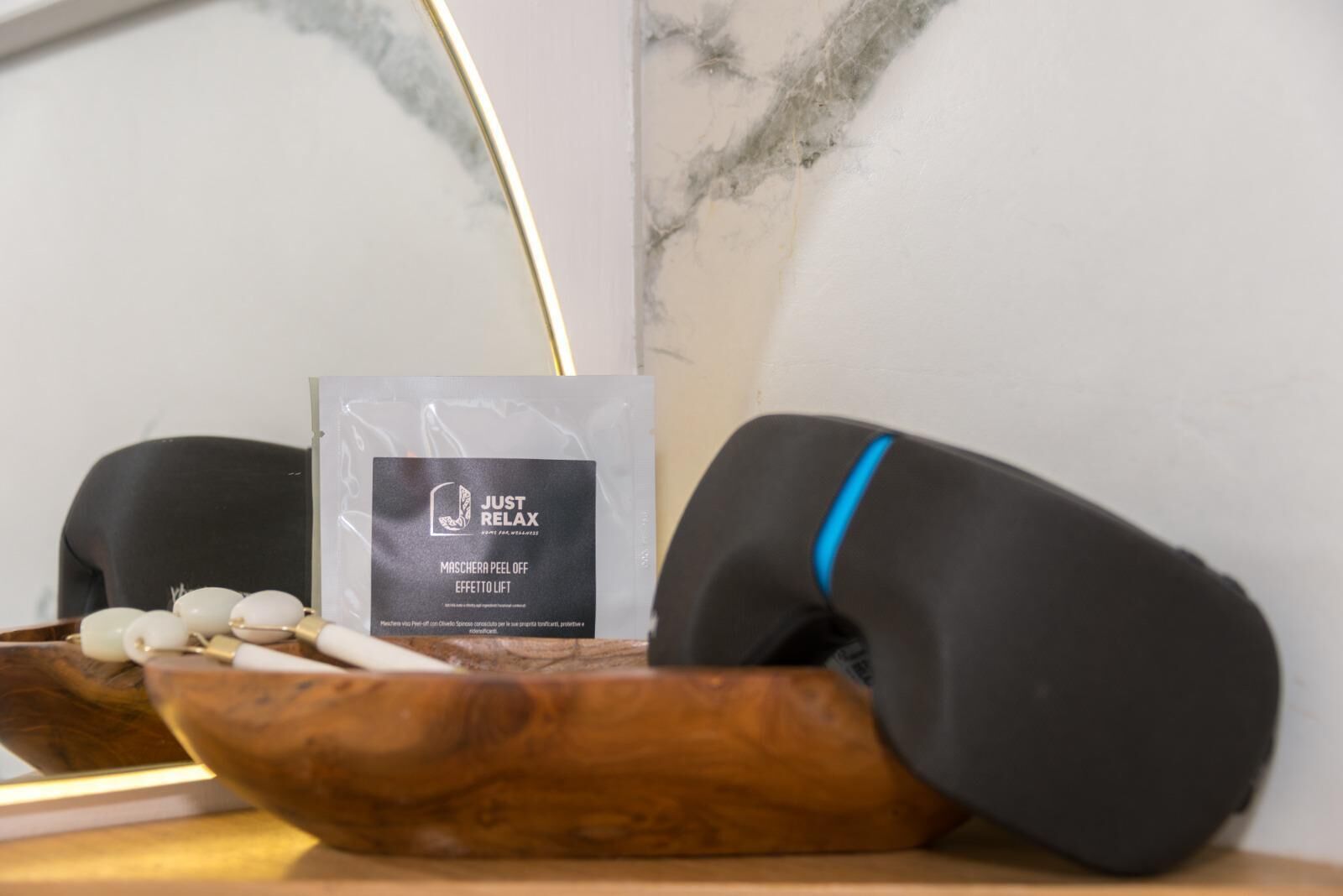 A massage chair with a black cushion and a blue accent, a wooden tray with stones, and a 'JUST RELAX' branded bag.