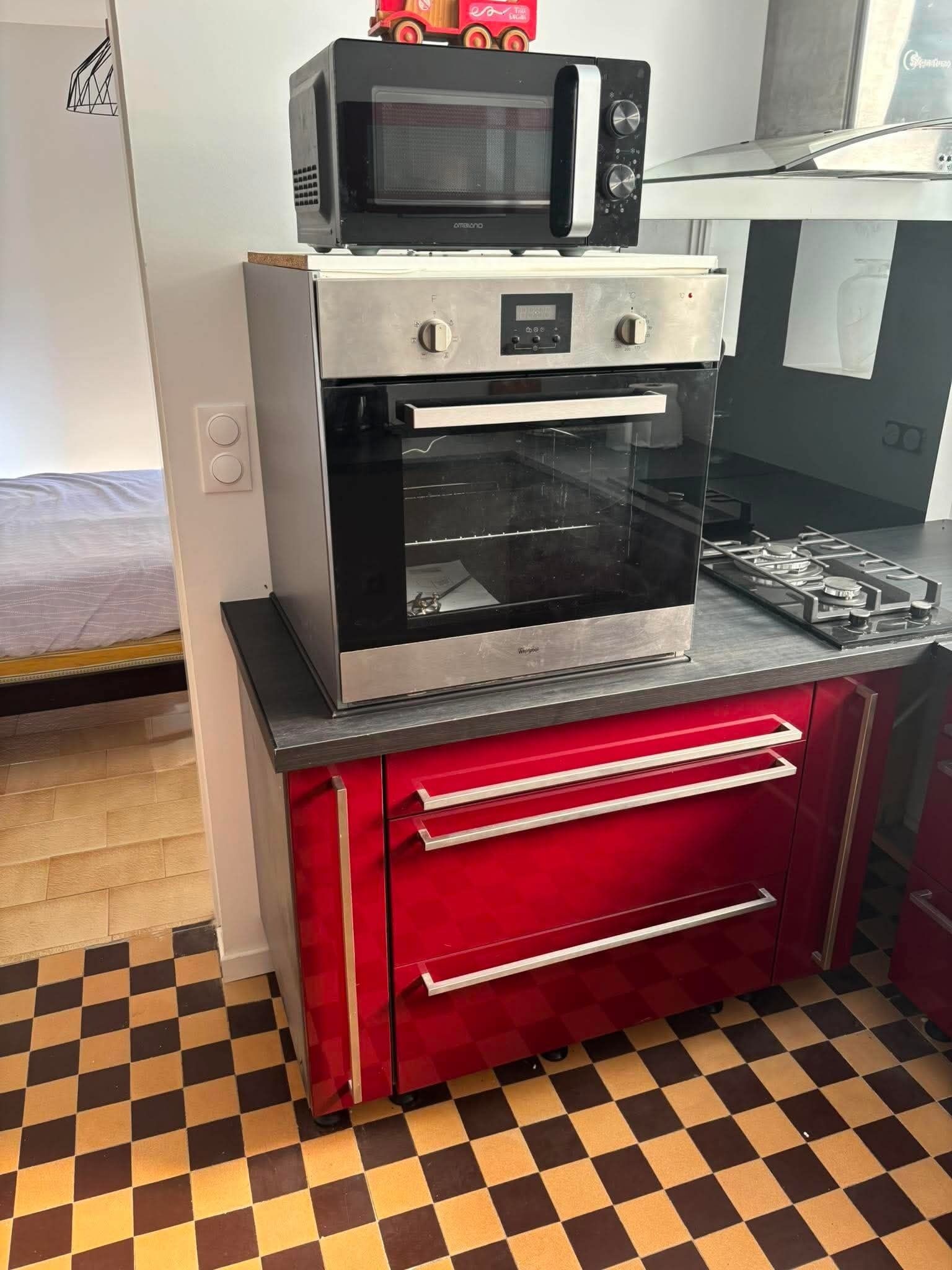 Une cuisine compacte équipée d’un four à micro-ondes, d’un four traditionnel et d’une cuisinière à gaz, le tout installé sur un plan de travail noir.