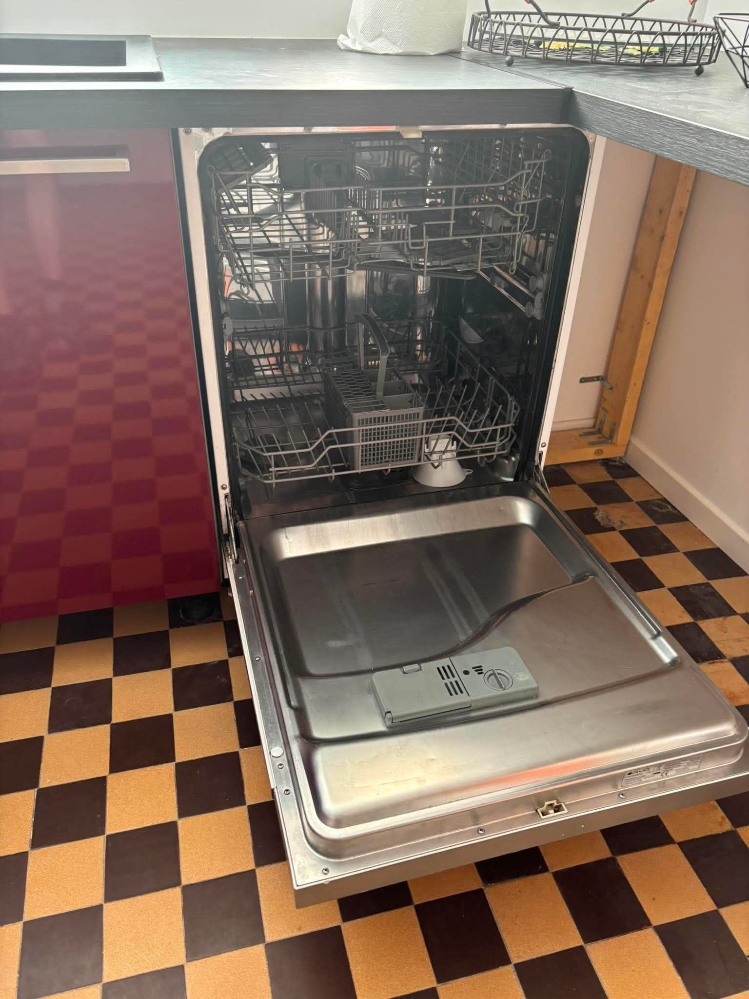 Eine offene Spülmaschine mit Schachbrettmuster auf dem Boden und einem roten Schrank.