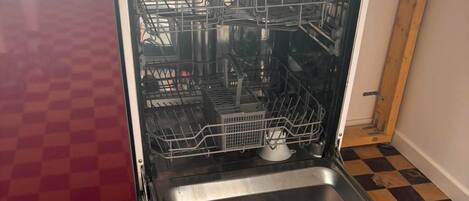 Eine offene Spülmaschine mit Schachbrettmuster auf dem Boden und einem roten Schrank.