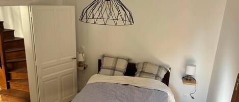Ein Schlafzimmer mit einem Bett, einem Schachbrettmuster-Boden, einer Holztür, einer Treppe, einer Pendelleuchte und einem Nachttisch mit einer Lampe.