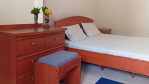 Um quarto com uma cama de madeira, uma mesinha de cabeceira, um penteado com gavetas e um banco.