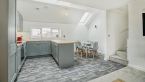 Eine moderne Küche mit grauen Schränken, einer Holztischplatte und einem Essbereich mit Tisch und Stühlen.