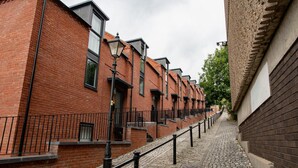 Eine enge Kopfsteinpflasterstraße, begrenzt von roten Backsteinbauten mit schwarzen Geländern und Straßenlaternen.