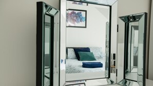 Ein Zimmer mit Spiegel, einem Bett, Kissen und einem gerahmten Bild an der Wand.