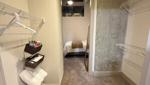 Ein Flur, der in ein Schlafzimmer mit Bett, einen Schrank mit Kleiderhaken und eine kleine Sitzecke mit einem Korb führt.