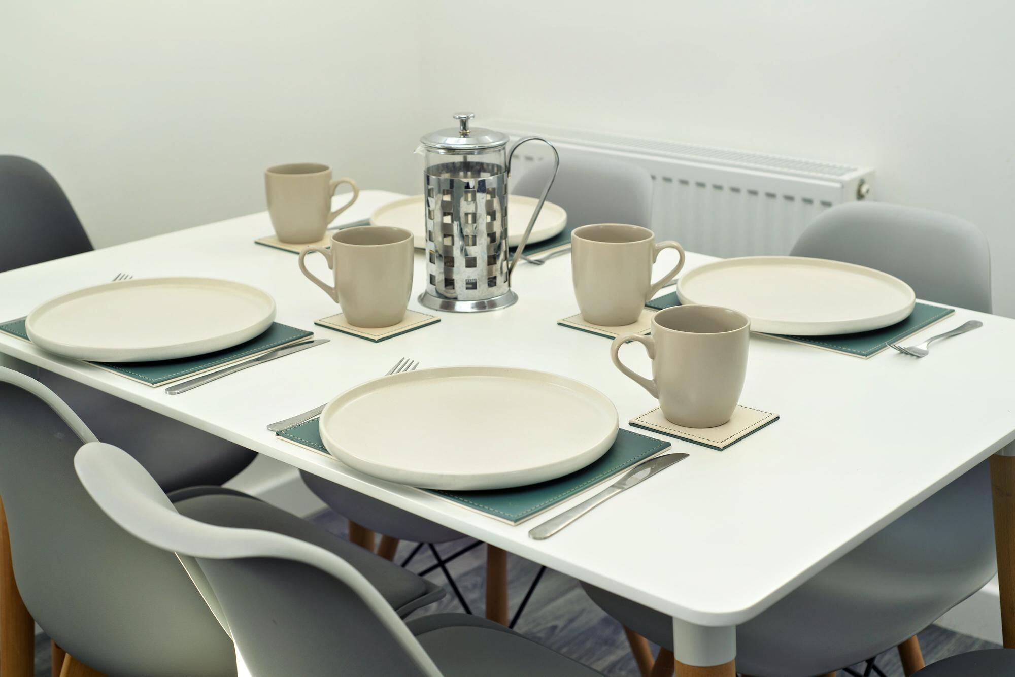 A dining table set with plates, cups, and a coffee pot, surrounded by chairs.