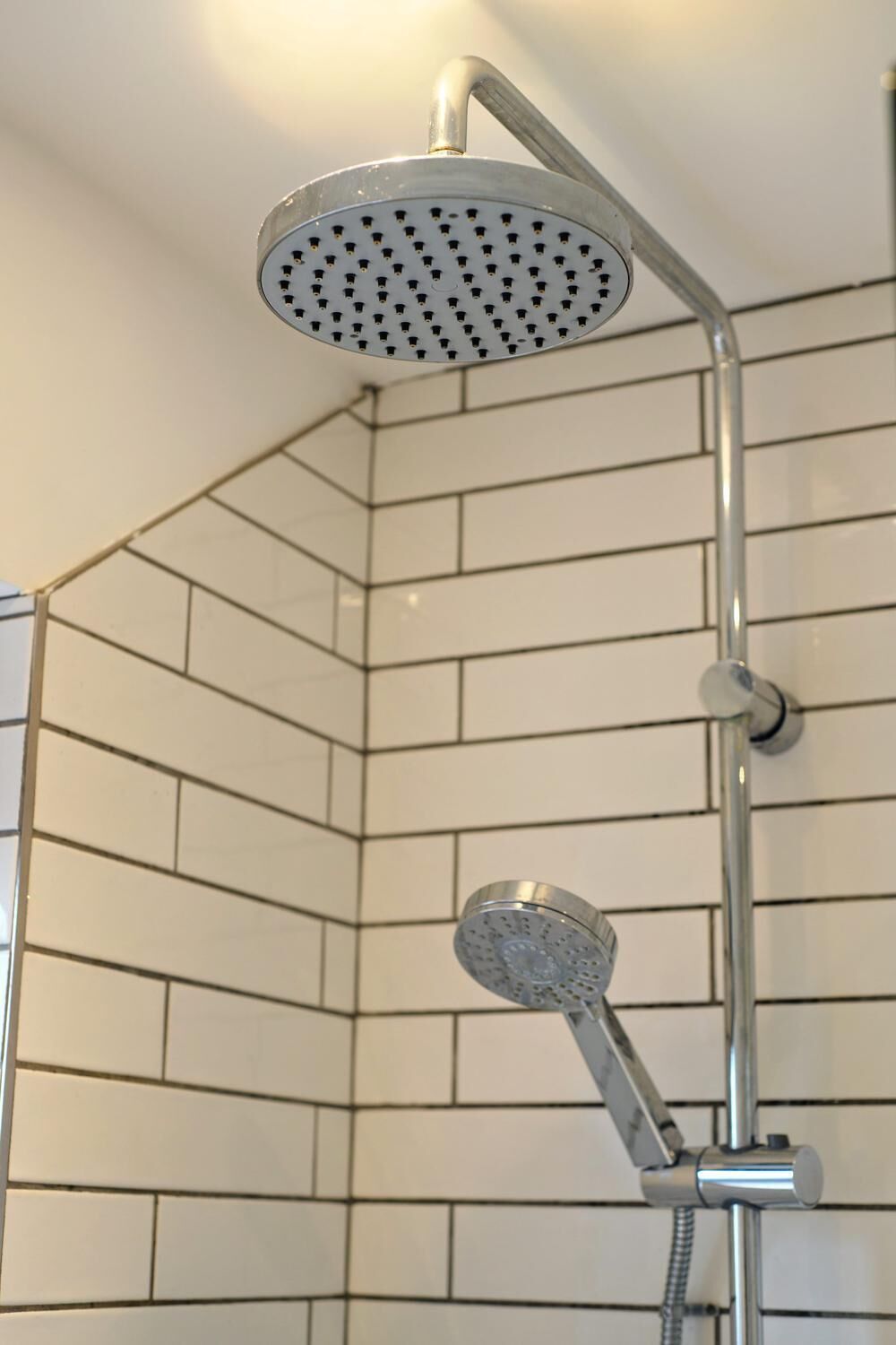 A shower with a handheld showerhead and a fixed overhead showerhead in a corner with white tiled walls.