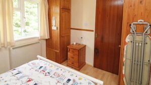 Ein Schlafzimmer mit einem Bett, einem Holzschrank, einem kleinen Schminktisch, einem Heizkörper und einem Fenster mit Vorhängen.