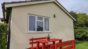 Ein kleines Gebäude mit einem Fenster, einem Tisch mit Bänken und einer Weinflasche.