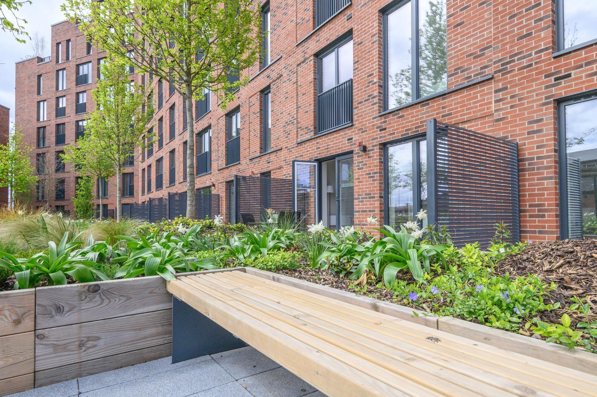 A modern brick building with large windows and a wooden bench in a landscaped area.
