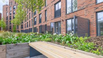A modern brick building with large windows and a wooden bench in a landscaped area.