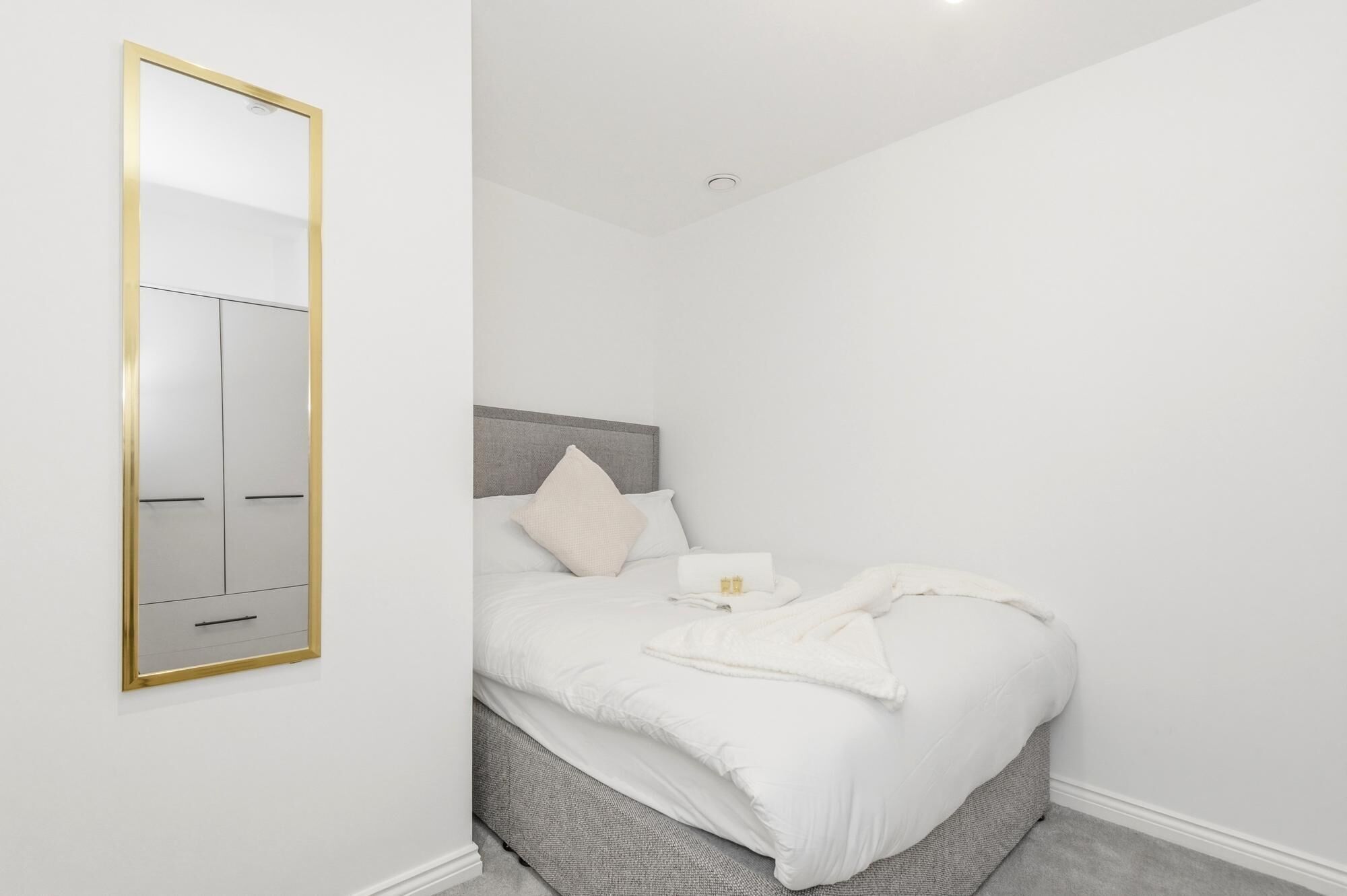 A bedroom with a bed, a bedside table, a mirror, and a ceiling light.