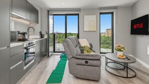 Un apartamento moderno con cocina, un sofá gris, una mesa de comedor y un balcón con vistas.