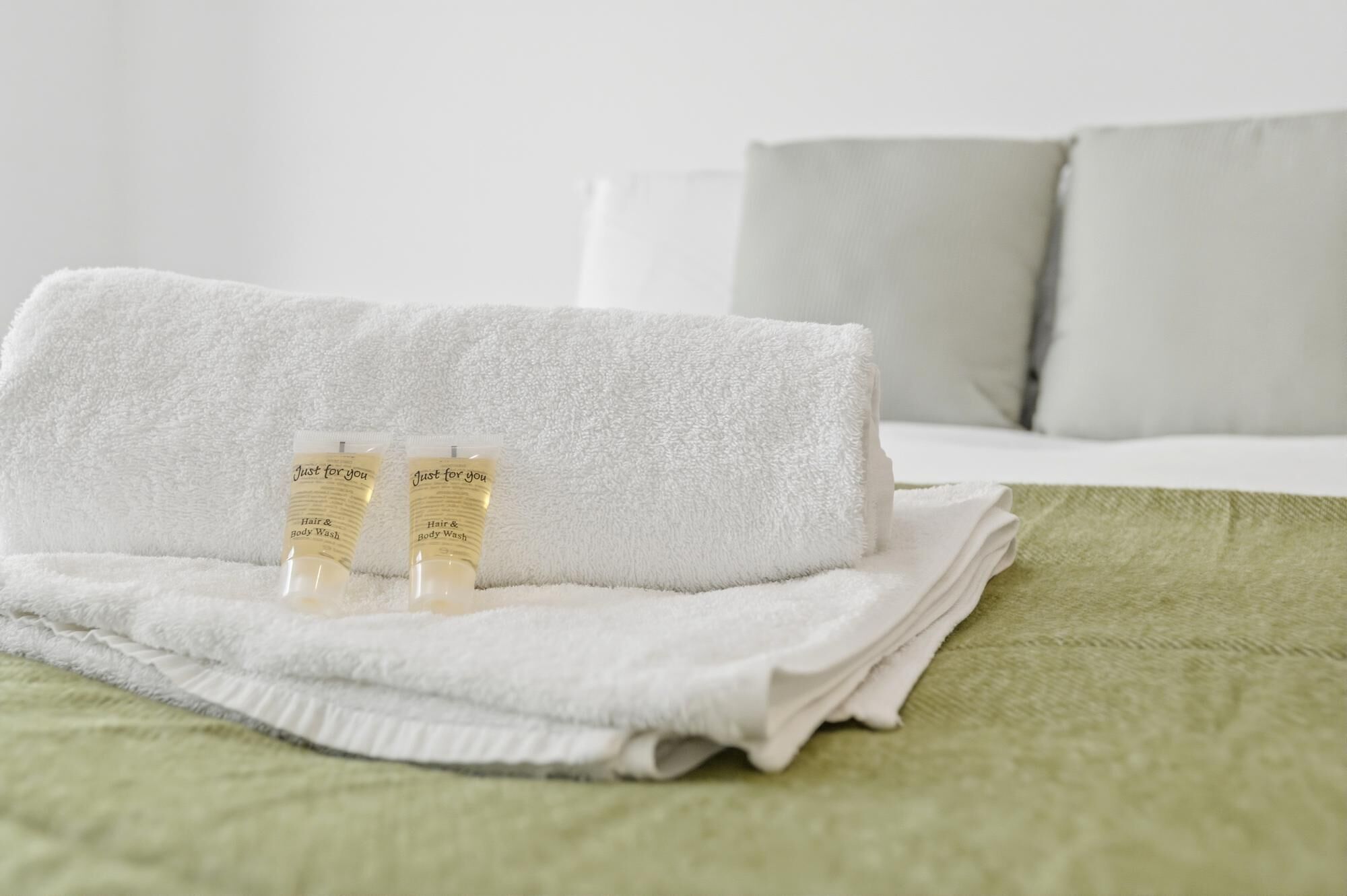 Ein ordentlich gemachtes Bett mit einer grünen Decke, zwei Flaschen Ha- und Körperpflege und ein weißes Handtuch.