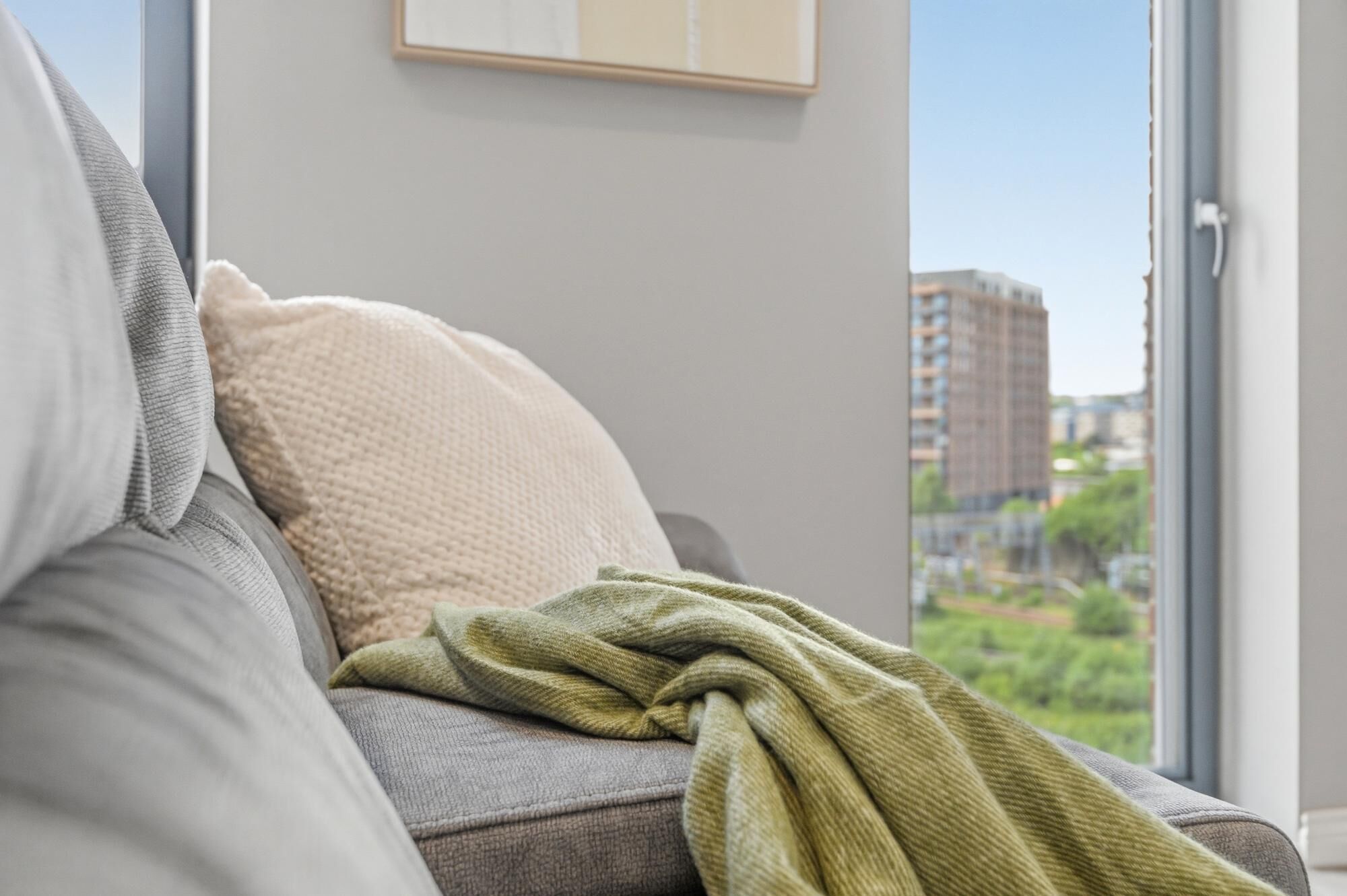 A modern living room with a grey sofa, a beige throw pillow, and a green blanket.