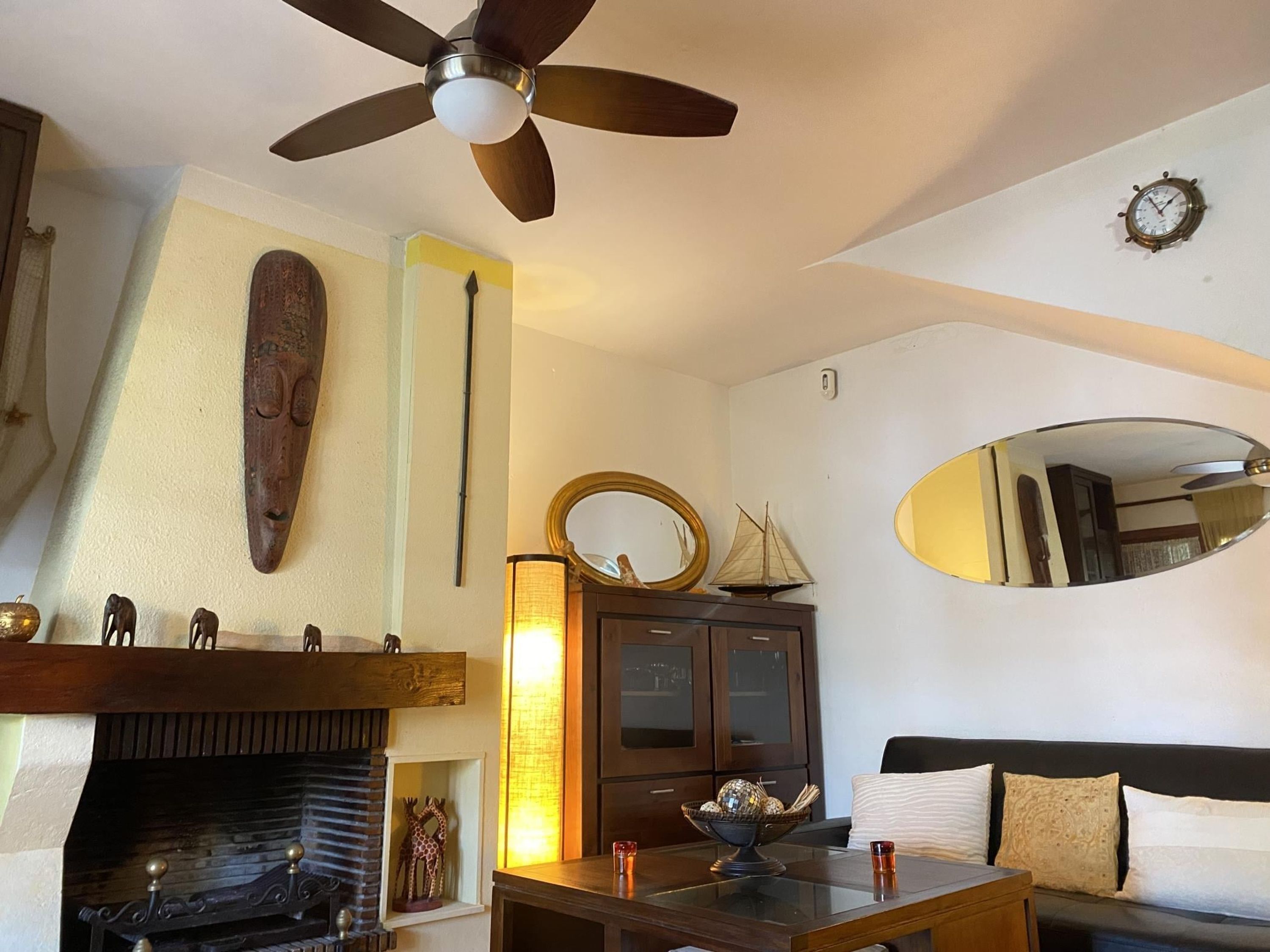A living room with a fireplace, a ceiling fan, a clock, and a mirror.