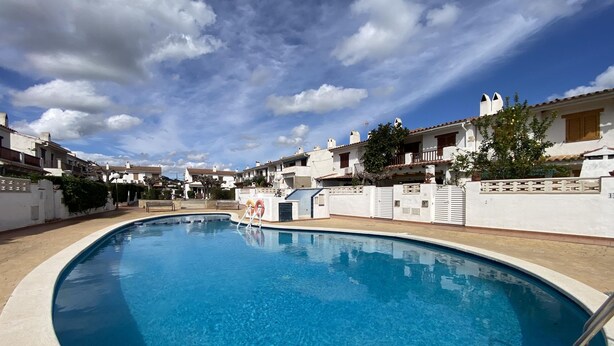 Una piscina envoltada d'edificis blancs amb balcons, sota un cel amb núvols dispersos.