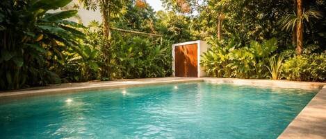 A swimming pool surrounded by lush greenery and a wooden structure.